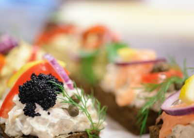 Close-up of Danish smørrebrød topped with creamy shrimp salad, black caviar, red onion, lemon, dill and capers, served on dark rye bread.