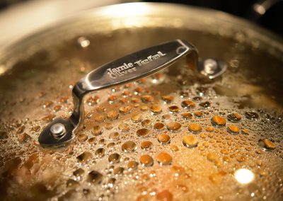 Close-up of a Jamie Oliver Tefal saucepan lid covered in condensation droplets, reflecting the warm kitchen light.