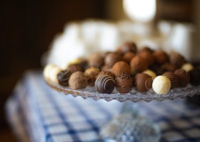 Assorted chocolate truffles and pralines arranged on a glass pedestal tray, captured with shallow depth of field and soft indoor lighting.